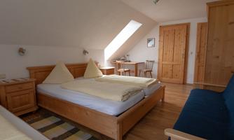 A cozy bedroom with two beds and wooden furniture. The walls are bright, and a window provides plenty of light.
