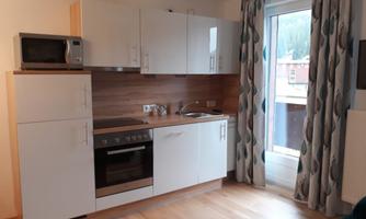 A modern kitchen with white cabinets and a wooden countertop. The kitchen is bright and has a window with curtains.