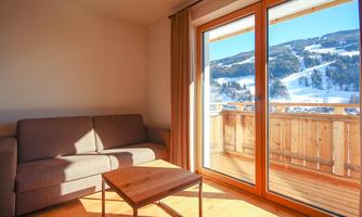 A bright room with a sofa and a table. Large windows offer a view of snow-covered mountains.