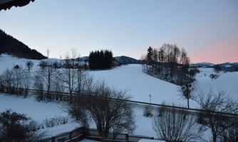 A snowy landscape with gentle hills and a clear sky. Trees and bushes surround the scene, which is set in a tranquil winter atmosphere.