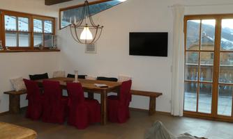A cozy dining area with a wooden table and red chairs. Large windows let in a lot of light and offer a view outside.