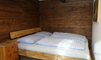 A cozy bedroom with a wooden bed and two pillows. The walls are made of dark wood, creating a warm atmosphere.