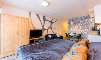 A modern room with two beds, a television, and a seating area. The walls are creatively designed, and the kitchen is visible in the background.
