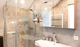 A modern bathroom with a walk-in shower and an elegant sink. The walls are in neutral colors and the floor is made of wood.