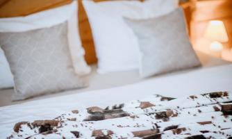 A cozy bed with white pillows and a warm blanket. The soft lighting creates a relaxed atmosphere.