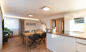 A modern living room with a dining area and an open kitchen. Bright colors and plenty of daylight create an inviting atmosphere.