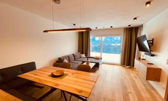 A modern apartment with a wooden table and a cozy couch. Large windows offer a view of the mountains.