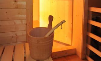 A wooden bucket with a wooden ladle stands in a sauna. In the background, the entrance to the sauna is visible with warm light.
