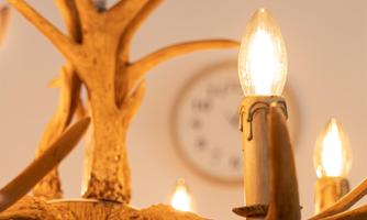 A decorative chandelier made of antlers with multiple light sources. In the background, a clock is visible on the wall.