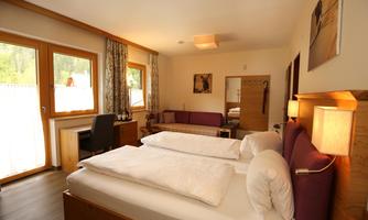 A cozy hotel room with two single beds, a sofa, and a desk. Large windows provide plenty of natural light.