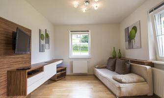 A modern living room with a comfortable sofa and a wood-decor wall. Large windows provide plenty of natural light.