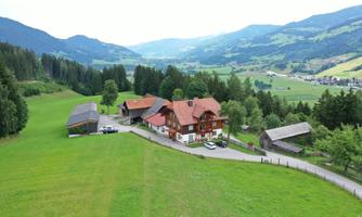 A picturesque landscape with a farmhouse and expansive green meadows. The mountains in the background add to the serene atmosphere.