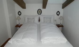 A cozy bedroom with a double bed, white bedcovers, and two nightstands. The walls are plain, and there are charming wall mirrors.