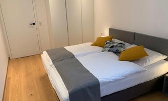 A modern bedroom with two beds and colored cushions. The floor is made of wood and there is a large mirror on the wall.