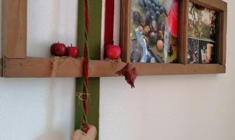 A rustic wooden picture frame with a decorative ribbon in red and green. It contains photos and small red apples as decoration.