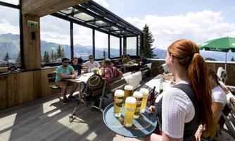A server is carrying a tray of beer in a mountain restaurant. In the background, guests are sitting and enjoying the view.