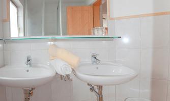 A bright bathroom with two sinks and a large mirror. Towels are neatly placed between the sinks.