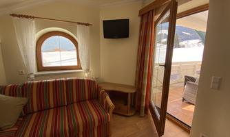 A cozy living space with a striped sofa and a window that opens to a balcony with a beautiful view. The atmosphere is bright and welcoming.