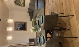 A modern living and dining room with an elegant table and cozy chairs. In the background, there is a comfortable couch and a decorative picture on the wall.