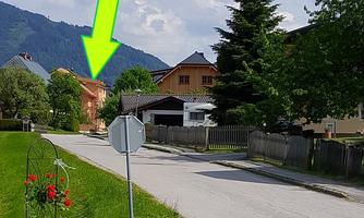 A quiet stretch of street with green lawn and some trees. In the background, houses and mountains can be seen.