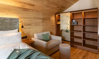 A modern hotel room with wood paneling and a cozy armchair. The room is bright and inviting, with a mirror and a small table.
