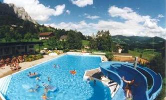 A beautiful pool with a giant slide in a green landscape. People enjoy the water and the sunny atmosphere.