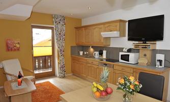 A modern kitchen with wooden cabinets and a dining table. On the table are fresh fruit and a bouquet of flowers.