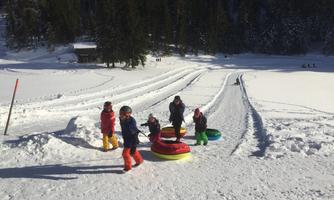 A winter landscape with snow and trees in the background. Children are playing with tires and having fun sledding.