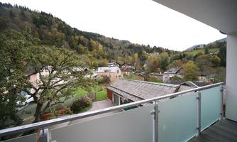 A view from a balcony of an idyllic landscape. In the background, there are hills and colorful trees, while in the foreground several houses stand.