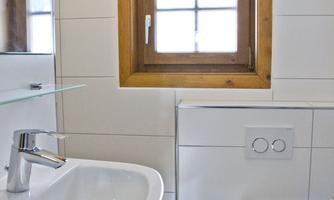A modern bathroom with a sink and a toilet. The window lets in natural light and creates a bright atmosphere.