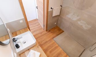 A modern bathroom with a sink and an open shower. The floor is made of wood, and the walls are bright and neutral.