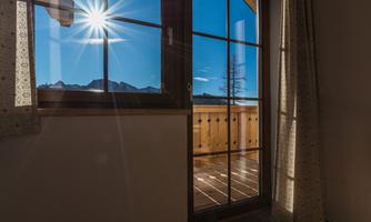 A bright room with a window that offers a sunny view of the mountains. The sun shines through the window, creating a warm ambiance.