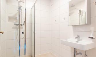 A modern bathroom with a glass shower enclosure and a simple sink. The walls are tiled, and there is a large mirror.
