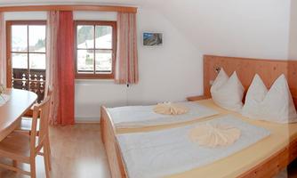 A cozy bedroom with two single beds and wood paneling. Windows with a view and a small table complete the picture.