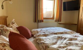A cozy bedroom with a large bed, covered with floral bedding. There is a view from the window and a television on the wall.