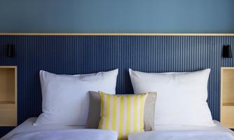 A modern bedroom with two large white pillows and a decorative pillow in yellow and white stripes. The wall is painted in a calming blue.