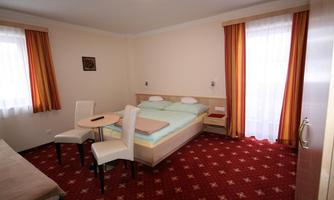 A simple hotel room with a double bed and a small table. The walls are light, and the curtains are in warm colors.