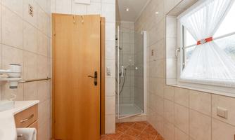A modern bathroom with bright tiles and a shower. A wooden door and a window provide light.