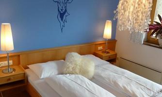 A cozy bedroom with a blue mural of a deer antler. The lighting consists of modern lamps and a striking fixture over the bed.