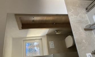 A modern bathroom with a bright, neutral color scheme. In the background, a window and a wooden door can be seen.