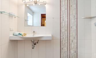 A modern bathroom with a white wall, a sink, and a large mirror. Towels in blue and yellow are placed on the shelf.