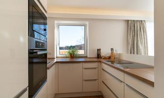 A modern kitchen with bright cabinets and a wooden countertop. The large window offers a view outside and lets in plenty of light.