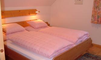A cozy bedroom with a double bed and pink bedspreads. The walls are bright and there is a small rug on the floor.