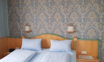 A cozy bedroom with two single beds and blue bedding. The walls are decorated in an elegant pattern.