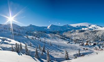 A beautiful winter landscape with a bright blue sky and snow-covered mountains. In the foreground, there are snow-covered trees and a small village.