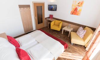 A modern hotel room with a double bed and colorful seating furniture. The room has a bright, inviting atmosphere and a television.
