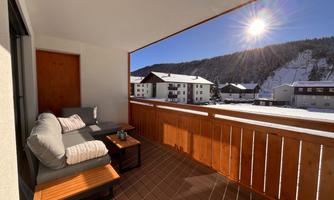 A beautiful balcony with a cozy seating area. In the background, you can see the snow-covered mountains and the sun shines clearly in the sky.