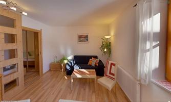 A bright living room with a sofa and a coffee table. Pictures hang on the wall, and a plant gives the room a cozy atmosphere.
