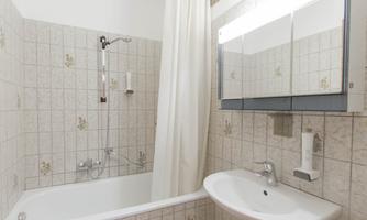 A bathroom with a bathtub and shower. The walls are tiled and a mirror is mounted above the sink.