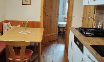A bright kitchen with a wooden floor and white cabinets. There is a table with chairs and a view of an adjacent room.